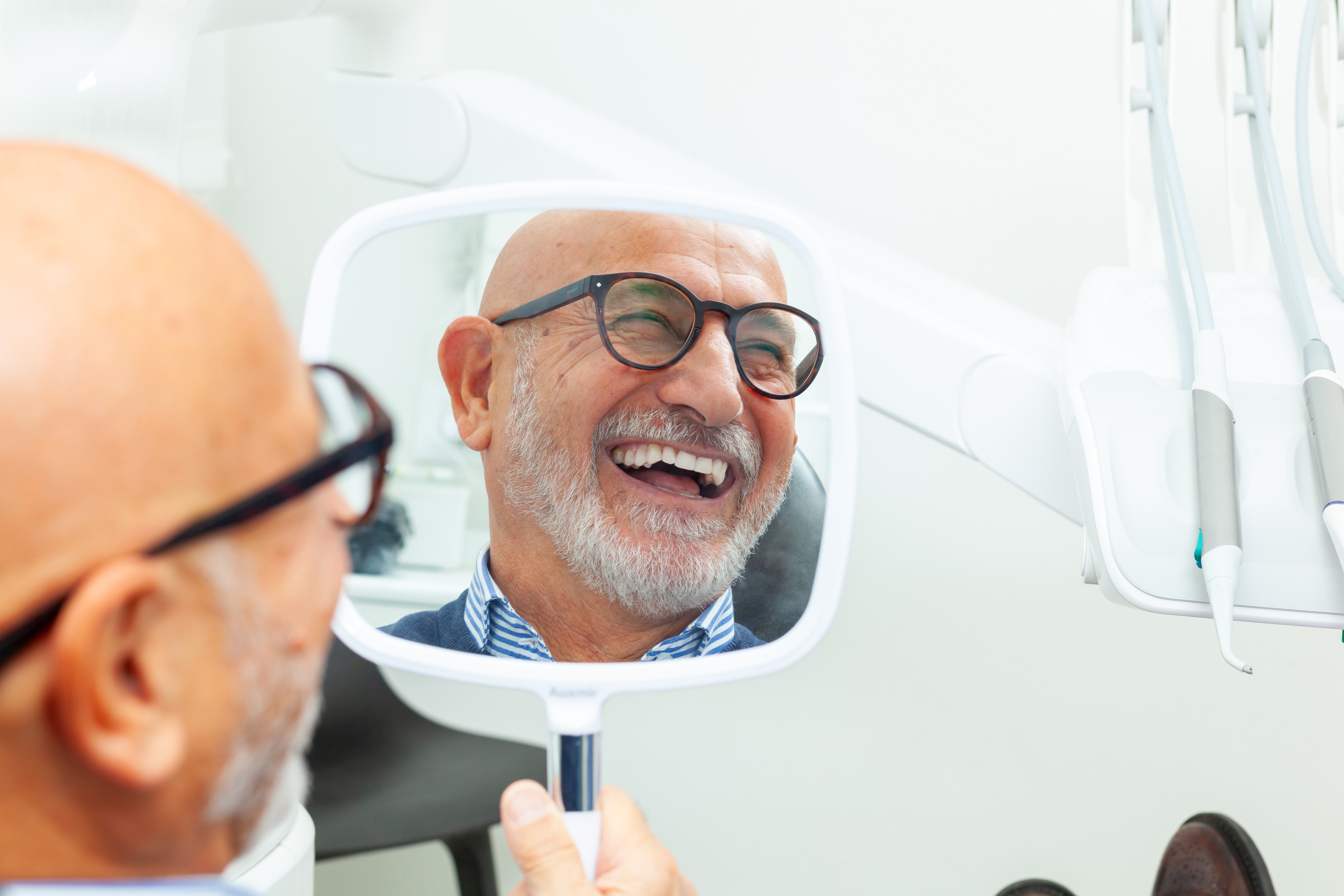 Man smiling showing his teeth looking in a mirror post dental procedure